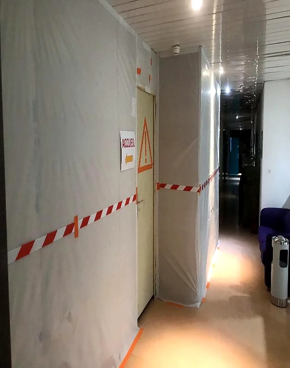 Cloison provisoire de confinement avec rubalise dans un couloir en activité